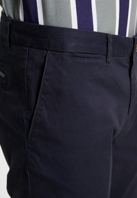 Mørkeblå shorts lavet af bomuld med en glat tekstur, der har en frontlomme og et lille mærkeskilt fastgjort til taljen.