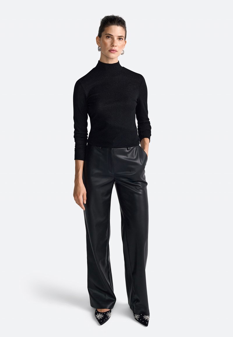 Črna oprijeta turtleneck majica iz mehkega materiala, kombinirana z ohlapnimi črnimi usnjenimi hlačami, okrašena z dekorativnimi črnimi petkami s dodatki.