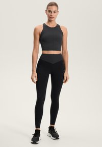 Čierny atletický crop top s textúrovaným vzorom rybej kosti, v kombinácii s čiernymi legínami s vysokým pásom. Nosené s čiernymi bežeckými topánkami.