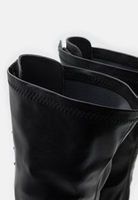 Czarne skórzane buty o gładkiej fakturze i widocznych szwach wzdłuż góry. Otwór jest szeroki, z zaokrąglonym brzegiem.