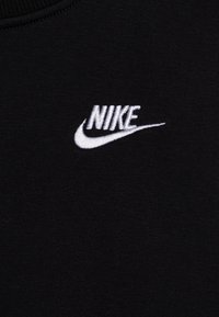 Svart stoff med en hvit brodert Nike-logo som har merkevarenavnet og swoosh-designet nær midten.