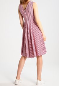 Robe sans manches à rayures rouges et blanches avec dos en V, jupe évasée et un détail de bouton à la taille, associée à des baskets blanches.