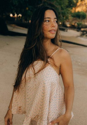 Jasnoróżowy top bez rękawów wykonany z miękkiego materiału, o luźnym kroju, zdobiony kolorowymi, nakrapianymi wzorami i falbaną na dole.