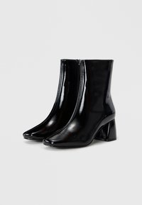 Schwarze Lackleder-Stiefeletten mit spitz zulaufenden Zehen, seitlichen Reißverschlüssen und Blockabsätzen. Glatte Textur und eleganter Schnitt.