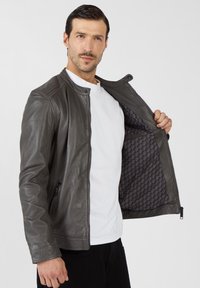 Ciemnoszara skórzana kurtka z zamkiem na froncie, żeberkowanym zdobieniem na ramionach i wzorzystą czarną podszewką. Noszona na białej koszulce.