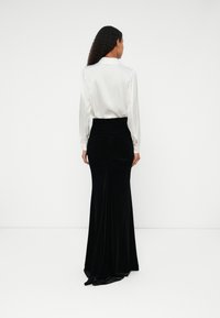 Saia longa de veludo preto com uma cintura ajustada e franzida. Combinada com uma blusa de seda branca com punhos abotoados.