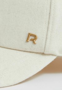 White wool cap featuring a gold "R" logo, with visible stitching and a curved brim. Soft texture and simple design elements.