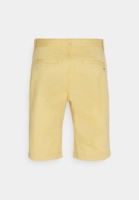 Pantaloni corti in cotone giallo chiaro, di media lunghezza e taglio dritto. Presentano due tasche posteriori e un logo discreto sul retro. Texture liscia.