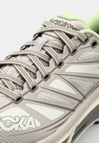 Light grey running shoe with mesh upper, green accents, and flat laces. Features molded details and a cushioned sole for comfort.
