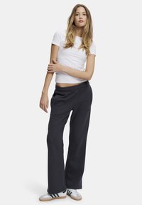 Svart joggebukser med elastisk livlinje og sidelommer, kombinert med en tettsittende hvit T-skjorte. Modellen står med armene krysset.