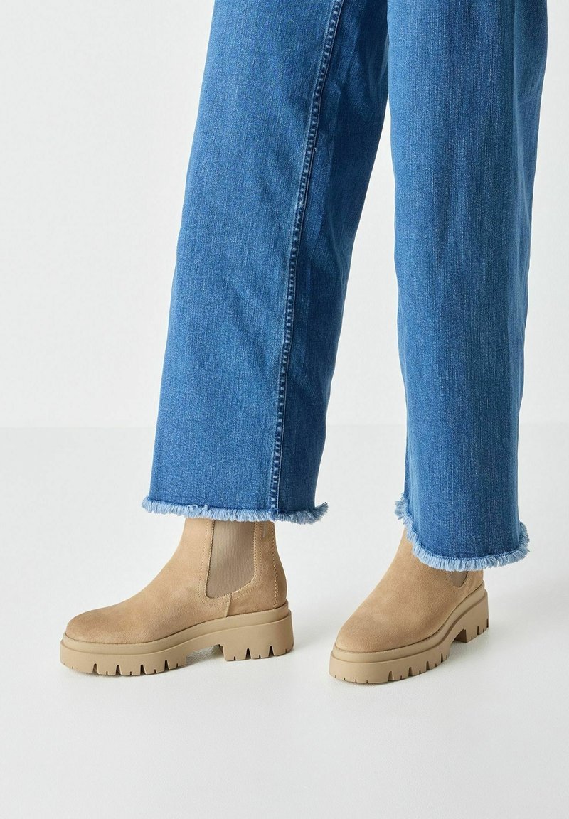 Bottes Chelsea en daim beige avec semelle épaisse, portées avec un jean en denim bleu aux bords effilochés.