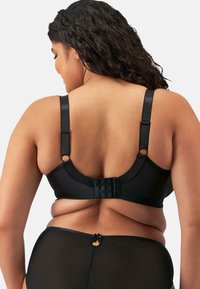 Musta rintaliivi leveillä olkaimilla, sileällä pinnalla ja hakaskiinnityksellä takana. Sopii yhteen läpikuultavien mustien alushousujen kanssa, joissa on nauha yksityiskohtana.