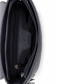 Tamsiai mėlynos odos krepšio vidus su tekstūruotu paviršiumi. Yra keli skyreliai, užtrauktuku užsegama kišenė ir prekės ženklo logotipas. Lygi audinio pamušalas.