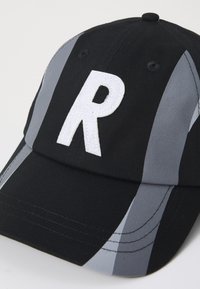 Casquette de baseball noire avec des rayures grises, un bord courbé et une lettre "R" blanche brodée sur le devant. Fabriquée en tissu texturé.