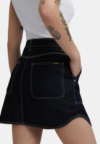 Gonna mini in denim scuro con vita alta, caratterizzata da cuciture a contrasto, due tasche posteriori e un discreto logo sul cinturino.