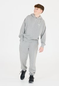 En grå hoodie och byxset i mjuk bomull, med avslappnad passform, ribbade ärmmuddar och logotyp på bröstet. I kombination med svarta sneakers.