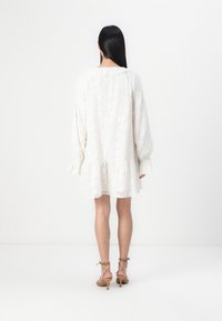 Λευκό φόρεμα με υφασμάτινο λουλουδάτο μοτίβο, άνετη γραμμή, μακριά μανίκια με φρου φρου μανσέτες και φούστα σε Α γραμμή. Φοριέται με ανοιχτό καφέ τακούνια με λουράκια.