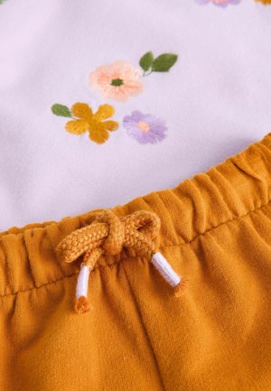 Katoenen top met geborduurde bloemmotieven in roze, oranje en paars. Geel-oranje elastische tailleband met een gevlochten trekkoord.