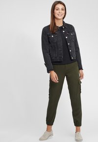 Giacca in denim nera, maglia a maniche lunghe nera, pantaloni cargo verde oliva con polsini elastici e scarpe grigie chiare con dettagli sottili.