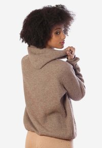 Maglione beige a coste con colletto alto, tessuto testurizzato e vestibilità morbida. Presenta spacchi laterali e spalle scese per una maggiore libertà di movimento.