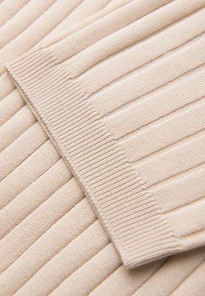 Beżowa prążkowana dzianina z zbliżeniem na mankiet rękawa pokazująca pionowe teksturowane linie i gładki, elastyczny ściągacz.
