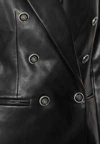 Veste blazer croisée en cuir noir avec des boutons argentés brillants et une texture lisse, dotée de revers crantés et de poches latérales.