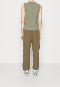 Ärmelloses Strickoberteil in Grün, kombiniert mit lockeren olivgrünen Cargohosen mit Seitentaschen und Sneakers mit grauen und gelben Akzenten.