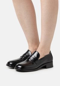 Sorte læder loafers med en glat finish, lav blokhæl og to dekorative forreste bånd. Designet til nemt at tage på.