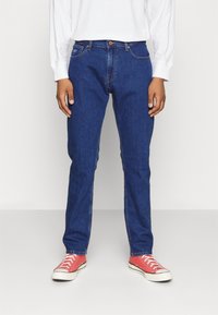 Jeans in denim blu con vestibilità dritta, cinque tasche e zip. Indossati con scarpe da ginnastica rosse, con lacci bianchi e suola in gomma.