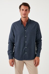 Camicetta blu con bottoni, realizzata in tessuto testurizzato, dotata di colletto a rema, maniche lunghe e bottoni bianchi, abbinata a pantaloni beige.