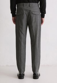 Graue Wollhose mit tailliertem Schnitt, flacher Vorderseite und schrägen Gesäßtaschen, kombiniert mit schwarzen Business-Schuhen.