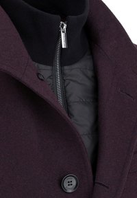 Burgundowy płaszcz z mieszanki wełny z czarną wewnętrzną warstwą na zamek, wysokim kołnierzem i wyraźnym czarnym guzikiem z przodu.