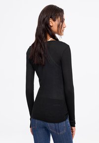 Black long-sleeve top made of stretchy, lightweight fabric. Features a rounded neckline and fitted design, paired with blue jeans.