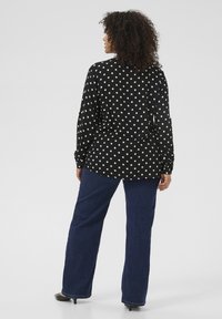 Czarna koszula zapinana na guziki w białe kropki, z długimi rękawami i luźnym krojem, w zestawie z niebieskimi spodniami typu wide-leg i czarnymi szpilkami.