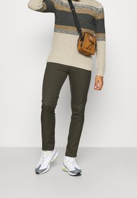Beige en grijs gestreepte gebreide trui, olijfgroene slim-fit broek en witte sneakers met grijze en limegroene accenten. Bruine crossbodytas.