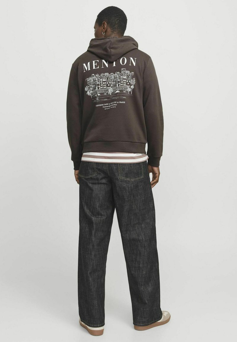 Sudadera marrón con gráfico de "MENTON" y edificios en la parte posterior, combinada con jeans oscuros de corte holgado y zapatillas beige. Textura áspera visible.