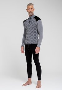 Termisk basislagstrøje i grå med mønstrede detaljer på brystet og sorte skulderakkenter, parret med sorte termiske leggings. Materialet ser strækbart ud.
