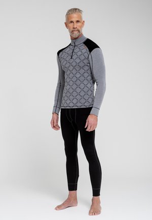 Termisk basislagstrøje i grå med mønstrede detaljer på brystet og sorte skulderakkenter, parret med sorte termiske leggings. Materialet ser strækbart ud.