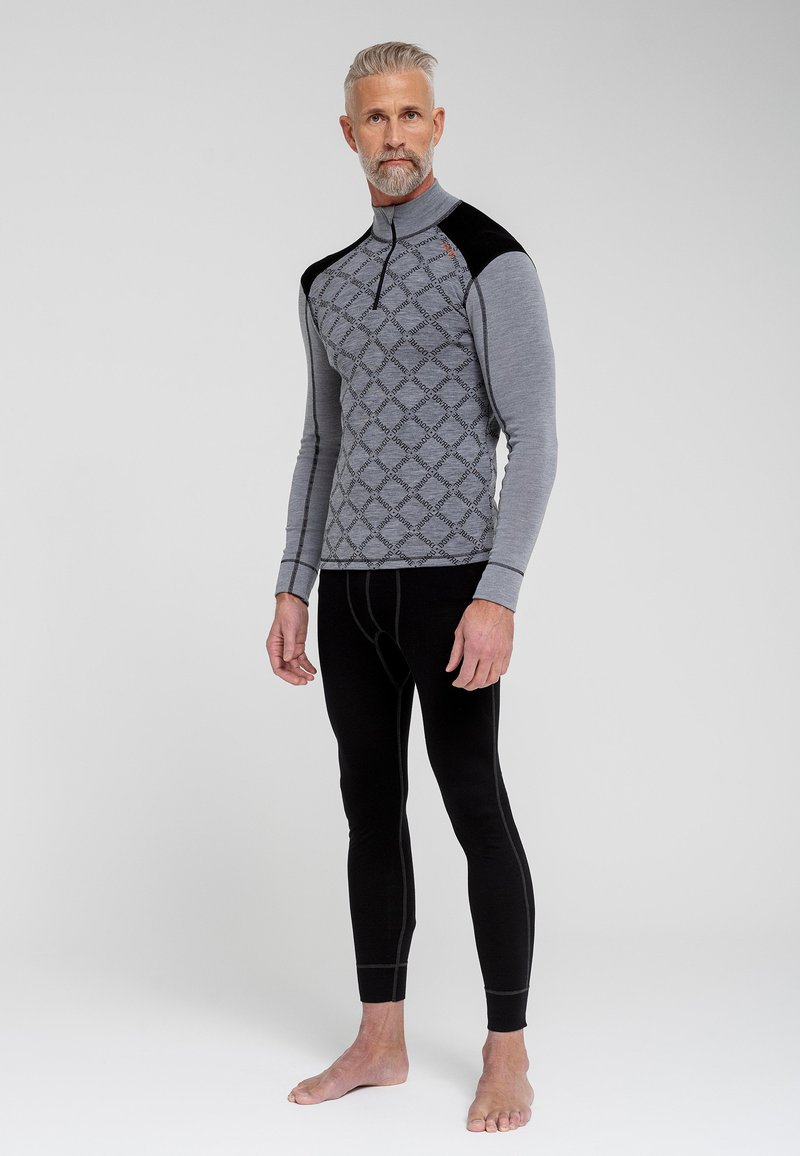 Termisk basislagstrøje i grå med mønstrede detaljer på brystet og sorte skulderakkenter, parret med sorte termiske leggings. Materialet ser strækbart ud.