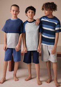 Kolme lasta pukeutuu rentoihin vaatteisiin: tummansininen paita harmaidenShortsien kanssa, harmaa paita laivastonsinistenShortsien kanssa ja raidallinen sininen paita harmaidenShortsien kanssa.