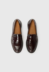 Braune Lederloafer mit glänzender Oberfläche, die einen genähten Riemen über die Oberseite, eine abgerundete Spitze und strukturierte Details auf dem Obermaterial aufweisen.