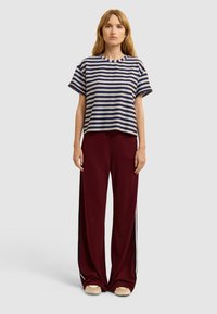Top de manga corta a rayas en azul marino y blanco, combinado con pantalones anchos burdeos con rayas laterales. Diseño casual con un ajuste holgado.