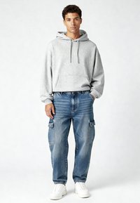 Grauer Kapuzenpullover mit Kängurutasche, kombiniert mit hellblauen Cargo-Jeans mit Seitentaschen, getragen mit weißen Sneakers.