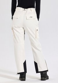 Person som bär off-white cargo-byxor med flera fickor och svarta förstärkta paneler på underbenen, tillsammans med svarta skor och svart topp.