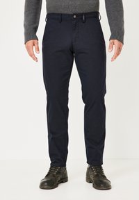 Marineblaue Chinos aus Baumwollmischung mit schlanker Passform, ausgestattet mit Knopfverschluss, Gürtelschlaufen und feiner Textur, kombiniert mit schwarzen Lederstiefeln.