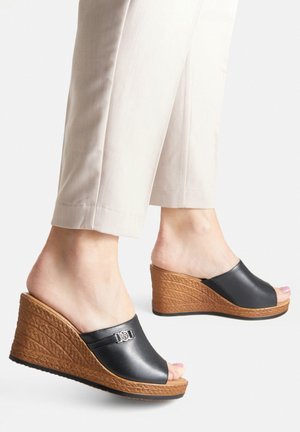 Čierne šľapky na klinovom podpätku s textúrovanou hnedou podrážkou, s hladkým koženým pásom a kovovým akcentom v hornej časti.