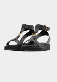 Μαύρα σανδάλια πλατφόρμας με σχεδιασμό T-strap, που διαθέτουν χρυσαφένιες μεταλλικές λεπτομέρειες και ρυθμιζόμενο κουμπί στον αστράγαλο. Υφή στη σόλα για καλύτερη πρόσφυση.