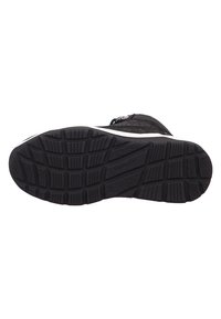 Semelle de chaussure noire avec caoutchouc texturé pour une meilleure adhérence, présentant un motif de crampons prononcé et un accent blanc le long du bord.