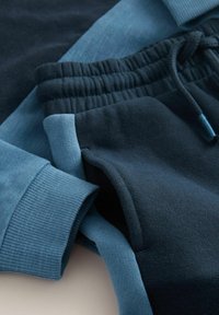 Pullover und Hose in verschiedenen Blautönen, mit einer Mischung aus glatten und gerippten Texturen, elastischem Bund und kontrastierenden Farbblöcken.