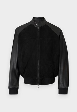 Czarna kurtka bomberka z rękawami z skóry, korpusem z zamszu, zapinana na suwak z przodu, kołnierzem na zatrzaski oraz ściągaczami na mankietach i dole.